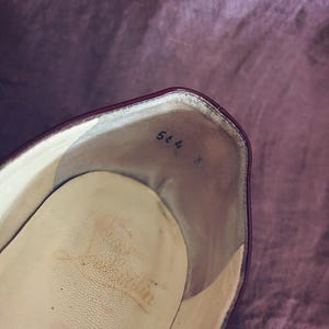 May include: Interior view of a burgundy leather shoe. The insole is a light beige with wear marks. Handwritten in black ink near the heel are the numbers "564" and "3".