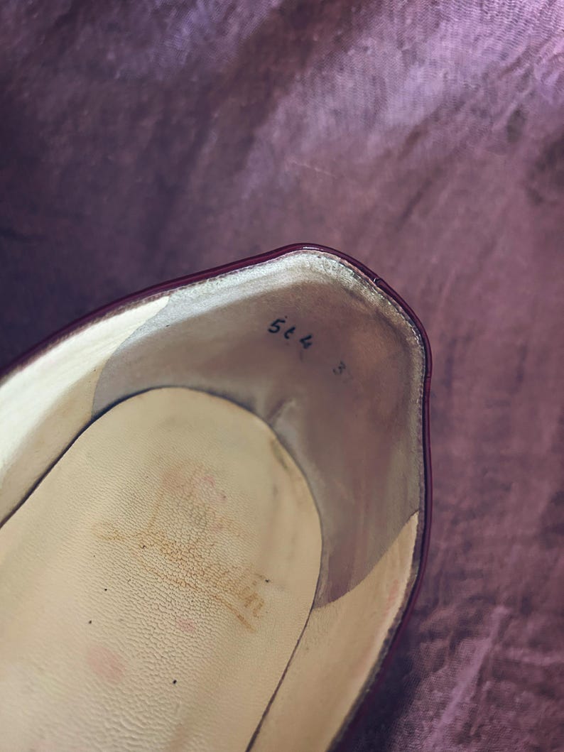 May include: Interior view of a burgundy leather shoe. The insole is a light beige with wear marks. Handwritten in black ink near the heel are the numbers "564" and "3".