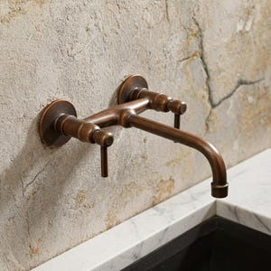 Puede incluir: Un grifo de pared de color bronce con dos manijas y un caño curvo. El grifo está instalado en una pared texturizada de color claro. El diseño tiene una estética vintage, adecuado para una cocina o un baño.