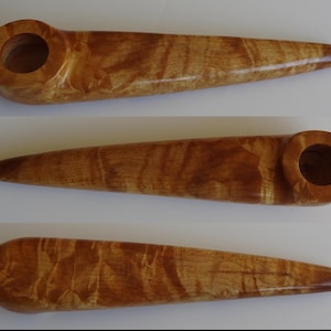 May include: A long, wooden pipe with a natural wood finish. The pipe has a wide, rounded bowl and a long, slender stem. The wood grain is visible and has a light brown color.