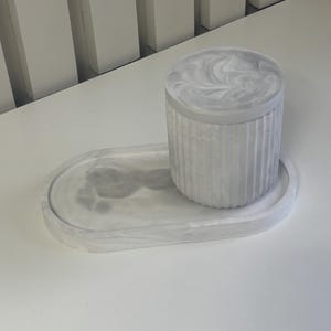 May include: A white marble-patterned oval tray with a white marble-patterned cylindrical container with a ribbed design.