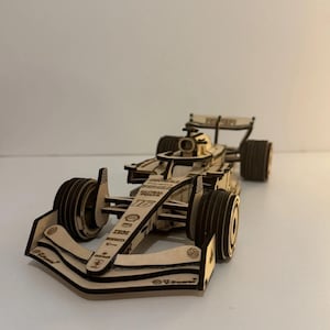 Puede incluir: Un modelo de coche de carreras de Fórmula 1 cortado con láser en madera, con el número 16 y varios logotipos de patrocinadores como Global Poker, Shell y V-Power. El modelo está construido en madera contrachapada clara con bordes visibles.