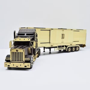 Könnte beinhalten: Ein Modell-Sattelzug aus hellen und dunklen Holzteilen. Der LKW verfügt über einen detaillierten Frontgrill, Seitenspiegel und einen langen Anhänger mit rechteckigen Paneelen sowie vertikalen Türgriffen an der Seite.