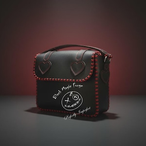 Puede incluir: Bolso de cuero negro con costuras rojas y detalles en forma de corazón. El bolso tiene un asa superior, un cierre de solapa y un diseño decorativo con el texto "Black Magic Forge" y "Perfectly Imperfect".