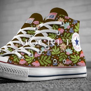 May include: High-top brown sneakers with a floral pattern featuring pink, blue, and green flowers and leaves. The sneakers have white laces, a white rubber sole, and a blue star logo on the side.