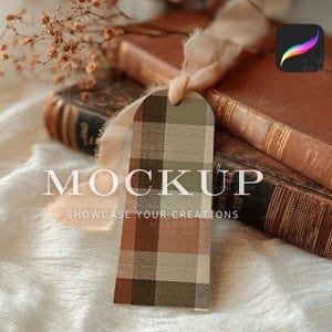 Può includere: Un'etichetta a quadri con la parola "MOCKUP" e la frase "SHOWCASE YOUR CREATIONS" stampata sopra. L'etichetta è appesa davanti a due libri antichi con copertine marroni. Un nastro e fiori secchi sono anche nell'immagine.