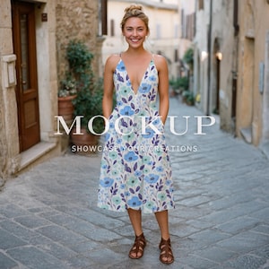 May include: A woman wearing a floral print dress with a deep V-neckline and spaghetti straps. The dress features blue and purple floral patterns on a white background. The text "MOCKUP SHOWCASE YOUR CREATIONS" is overlaid on the image. She is wearing brown sandals.