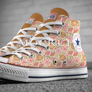 May include: High-top canvas sneakers with a floral pattern in shades of pink, orange, and green. The sneakers have white laces, a white rubber toe cap, and a brown tongue. The Converse logo is visible on the side.