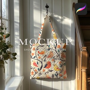 May include: A white tote bag with a quilted design and a floral pattern featuring colorful birds. The bag has black straps and is hanging on a hook.