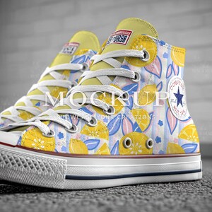 May include: High-top canvas sneakers with a vibrant lemon and leaf pattern. The sneakers feature white laces, a yellow tongue, and a white rubber sole with a blue stripe. The design includes the text "MOCKUP SHOWCASE YOUR CREATIONS".