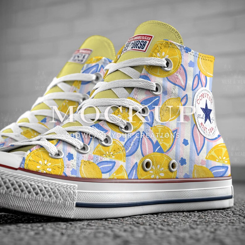 May include: High-top canvas sneakers with a vibrant lemon and leaf pattern. The sneakers feature white laces, a yellow tongue, and a white rubber sole with a blue stripe. The design includes the text "MOCKUP SHOWCASE YOUR CREATIONS".