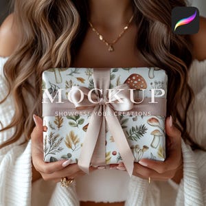 May include: A white gift box with a brown ribbon and a floral pattern featuring mushrooms, leaves, and berries. The box is wrapped in paper that says "MOCKUP SHOWCASE YOUR CREATIONS".