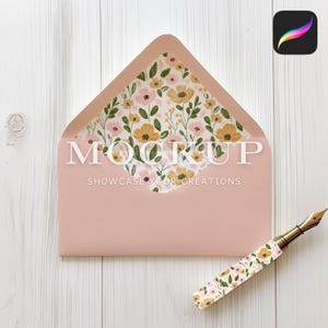 May include: A pink envelope with a floral pattern on the inside flap. The envelope is lying flat on a white wooden surface. A gold pen with a floral pattern is lying next to the envelope.