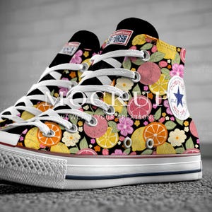 May include: High-top canvas sneakers with a vibrant floral and fruit pattern. The design features lemons, oranges, grapefruits, and flowers on a black background. The sneakers have white laces, a white rubber sole, and a Converse logo patch.