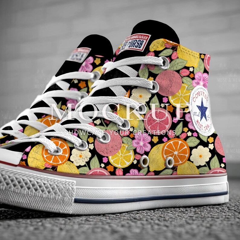 May include: High-top canvas sneakers with a vibrant floral and fruit pattern. The design features lemons, oranges, grapefruits, and flowers on a black background. The sneakers have white laces, a white rubber sole, and a Converse logo patch.