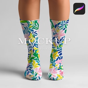 Op de afbeelding: Een paar witte sokken met een kleurrijk bloemenpatroon met roze, gele, groene en blauwe bloemen en bladeren. De sokken worden getoond op de benen van een model.