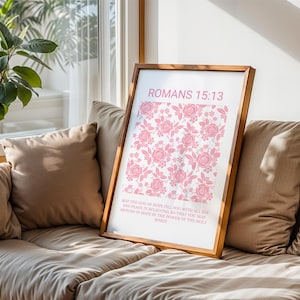Pu&ograve; includere: Una stampa incorniciata con un motivo floreale rosa e il testo "ROMANS 15:13". La stampa include un versetto biblico. La cornice &egrave; in un caldo tono legno e la stampa &egrave; esposta su un divano beige vicino a una finestra.