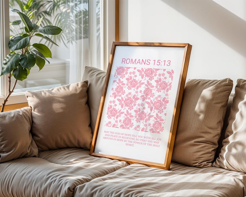 Pu&ograve; includere: Una stampa incorniciata con un motivo floreale rosa e il testo "ROMANS 15:13". La stampa include un versetto biblico. La cornice &egrave; in un caldo tono legno e la stampa &egrave; esposta su un divano beige vicino a una finestra.