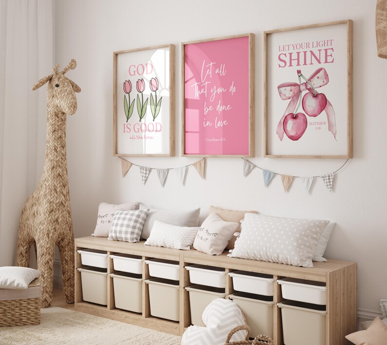 Pu&ograve; includere: Una scena di cameretta con opere d'arte incorniciate con citazioni e illustrazioni ispiratrici. Una grande giraffa tessuta &egrave; accanto a un mobile contenitore in legno con contenitori bianchi e beige. Cuscini e ghirlande decorative completano l'arredamento della stanza.