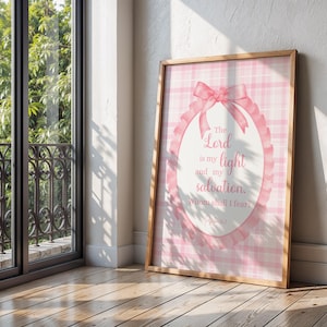 Pu&ograve; includere: Una stampa incorniciata con uno sfondo a quadri rosa e bianchi. La stampa presenta un design ovale con un fiocco rosa e il testo "The Lord is my light and my salvation, Whom shall I fear?" in un carattere corsivo. La cornice &egrave; in legno.