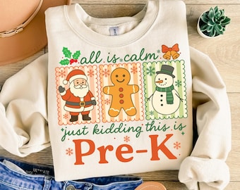 Könnte beinhalten: Cremefarbenes Pre-K-Sweatshirt mit festlichem Design. Die Grafik zeigt den Weihnachtsmann, einen Lebkuchenmann und einen Schneemann mit dem Text "all is calm, just kidding this is Pre-K".