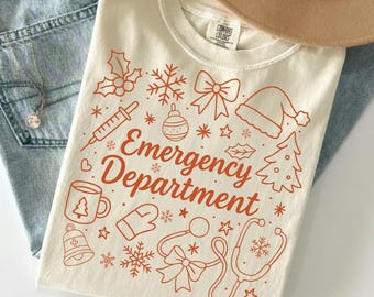 Könnte beinhalten: Cremefarbenes T-Shirt mit rotem Grafikdesign mit medizinischen Symbolen zum Thema Weihnachten und den Worten "Emergency Department". Das Design umfasst eine Spritze, ein Stethoskop und einen Weihnachtsbaum.