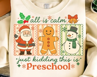 Könnte beinhalten: Cremefarbenes Sweatshirt mit festlichem Design. Die Grafik zeigt den Weihnachtsmann, einen Lebkuchenmann und einen Schneemann, zusammen mit dem Text "all is calm" und "just kidding this is Preschool". Das Design hat rote, grüne und orangefarbene Akzente.