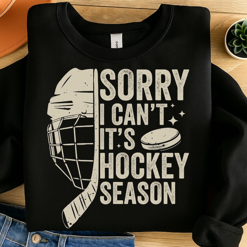 May include: Black sweatshirt with a hockey-themed graphic. The design includes a hockey helmet, a hockey puck, and the text "SORRY I CAN'T IT'S HOCKEY SEASON" in a distressed, vintage style. A great gift for hockey fans.