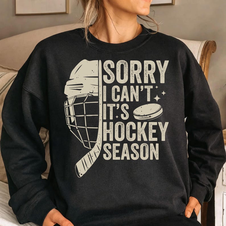 May include: Black sweatshirt with the text "SORRY I CAN'T IT'S HOCKEY SEASON" in a distressed, off-white font. A hockey helmet, stick, and puck graphic are on the left side. The sweatshirt is a crew neck style.