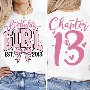 May include: White t-shirt with pink text and graphics. The front features "Birthday GIRL EST. 2013" with a bow. The back says "Chapter 13" with hearts and a butterfly. A birthday-themed tee.