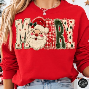 May include: A bright red crewneck sweatshirt featuring the word MERRY in large, textured letters. The letter M has red snowflakes, the letter E is replaced by a smiling Santa Claus face, the letter R has a red plaid pattern, and the letter Y features small green trees and red hearts.