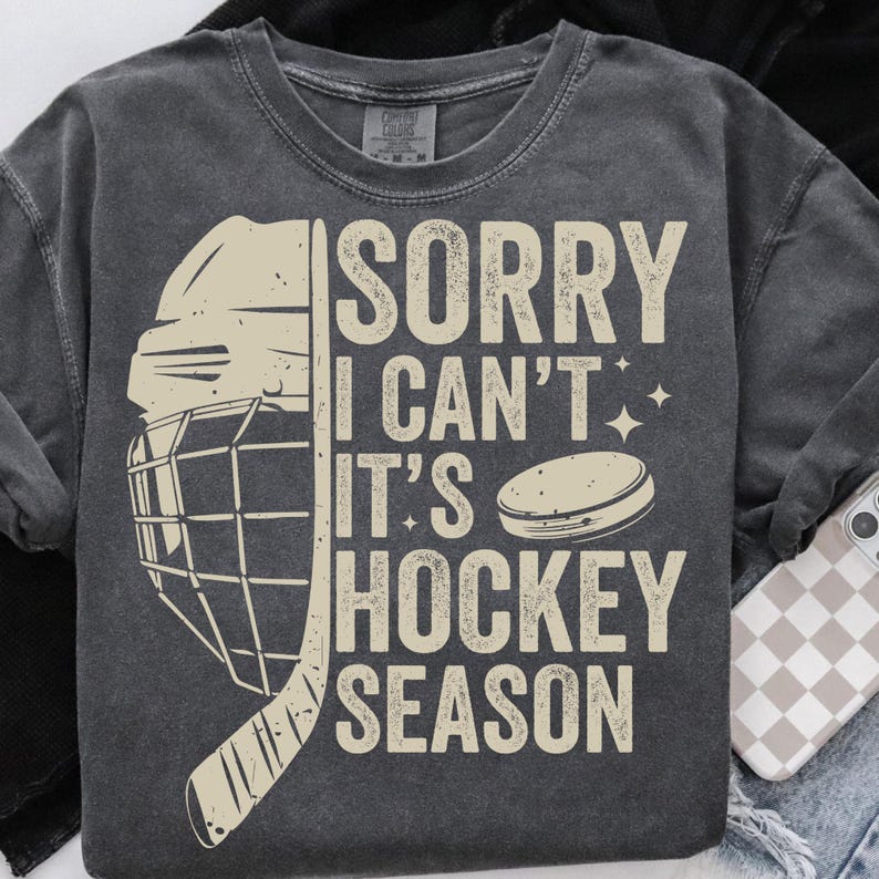 May include: Dark gray sweatshirt with the text "SORRY I CAN'T IT'S HOCKEY SEASON" in a distressed, off-white font. A hockey helmet, stick, and puck graphic are also featured in off-white.