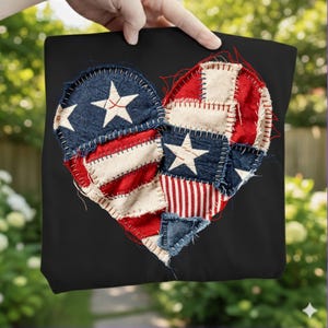 May include: A black tote bag with a heart-shaped design made from patchwork fabric. The heart features blue denim with white stars, red and white striped fabric, and off-white fabric. The patches are stitched together with red thread.