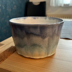 Könnte beinhalten: Eine Keramikschale mit einem Farbverlauf, der von hellem Beige am Boden zu Grün-, Blau- und Lilatönen am Rand übergeht. Die Schale hat eine leicht unregelmäßige Form und eine glatte, glasierte Oberfläche.
