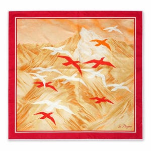 May include: A square scarf with a red border and a white inner border. The scarf features a mountain landscape in shades of orange and yellow, with red, white, and orange birds in flight. The text "La Plagne" is in the bottom right corner.