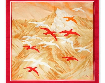 May include: A square scarf with a red border and a white inner border. The scarf features a mountain landscape in shades of orange and yellow, with red, white, and orange birds in flight. The text "La Plagne" is in the bottom right corner.