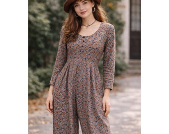 Puede incluir: Mono de manga larga con estampado floral en tonos azules, naranjas y marrones. El mono tiene un escote redondo y una botonadura frontal. Se lleva un sombrero marrón con un detalle floral.