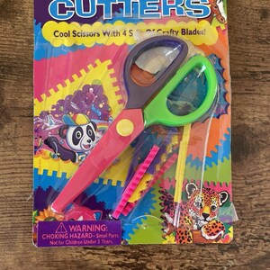 May include: A packet of craft scissors with a pink and green handle. The packaging features the word "CUTTERS" and the text "Cool Scissors With 4 Crafty Blades!" and a warning about small parts.