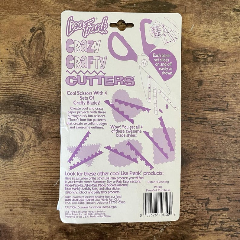 May include: A Lisa Frank Crazy Crafty Cutters package. The package features purple scissors with four sets of crafty blades. The text says, "Cool Scissors With 4 Sets Of Crafty Blades!" and "Wow! You get all 4 of these awesome blade styles!"