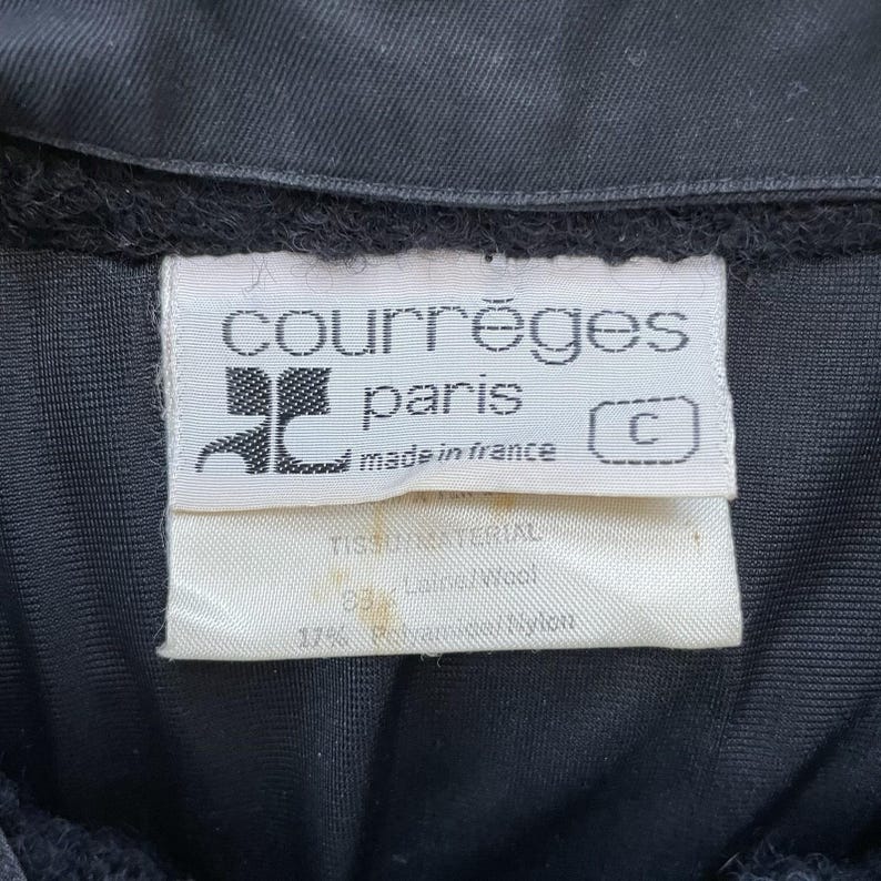 May include: Close-up of a black garment with a white label. The label reads "courr&egrave;ges paris made in france" with a logo. The label also lists the fabric composition: 83% Wool and 17% Polyamide/Nylon.