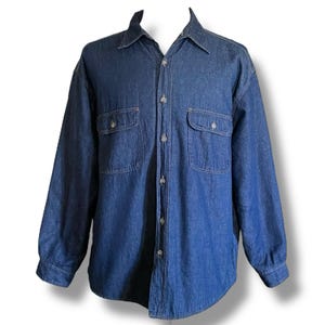 May include: A long-sleeved denim shirt in a medium blue wash. The shirt features two chest pockets with button closures, a classic collar, and button-down front. The sleeves have buttoned cuffs. The shirt is made of a sturdy denim fabric.