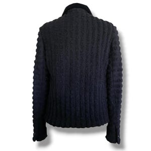 May include: A dark navy blue jacket with a textured, ribbed design. The jacket features a black velvet collar and buttoned cuffs. The back view showcases the vertical ribbed pattern and the tailored fit of the garment.