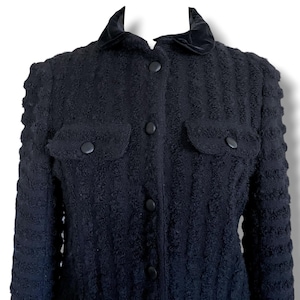 May include: A black textured jacket with a velvet collar and two front pockets. The jacket has a button-up closure and a textured pattern throughout the fabric. The jacket is a classic style.