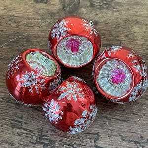 May include: Four vintage red Christmas ornaments with silver glitter accents. Each ornament has a clear, textured base with a pink and green interior. The ornaments are round and have a reflective, glossy finish.