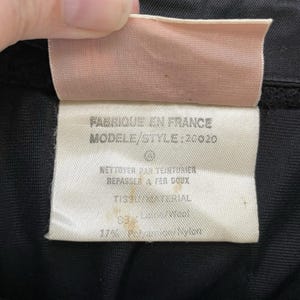 May include: Close-up of a clothing tag with text in French. The tag is white with black text and a pink top. The text includes "Fabriqu&eacute; en France" and "Mod&egrave;le/Style: 20020". The fabric is 83% wool and 17% polyamide nylon.