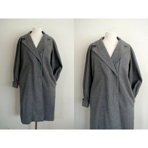 May include: A gray double-breasted wool coat with long sleeves and a collar. The coat has a slightly oversized fit and features a single button closure at the waist.