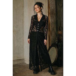 May include: A long-sleeved black lace duster coat featuring a notched lapel collar, a button-down front with four visible buttons, and a floor-length hemline. The garment is constructed from a sheer floral lace fabric with a solid black lining.