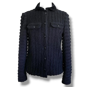 May include: A black textured jacket with a velvet collar and two front pockets. The jacket has a button-up closure and long sleeves. The fabric has a ribbed pattern, and the jacket appears to be a tailored fit.