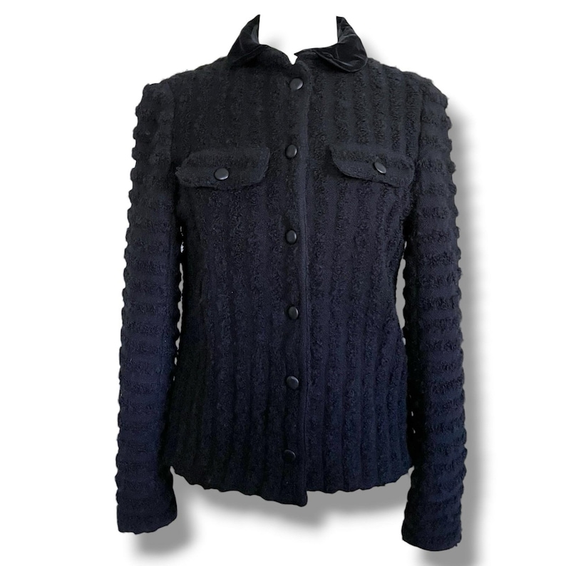 May include: A black textured jacket with a velvet collar and two front pockets. The jacket has a button-up closure and long sleeves. The fabric has a ribbed pattern, and the jacket appears to be a tailored fit.