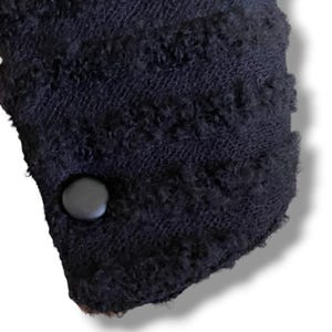May include: Close-up of a section of a dark navy blue knitted fabric with a textured, looped pattern. A dark gray button is attached to the fabric. The fabric has a soft, fuzzy appearance.